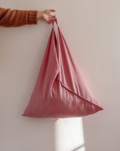 Różowa torba lniana origami o trójkątnym kroju bento bag trzymana w uniesionej dłoni.